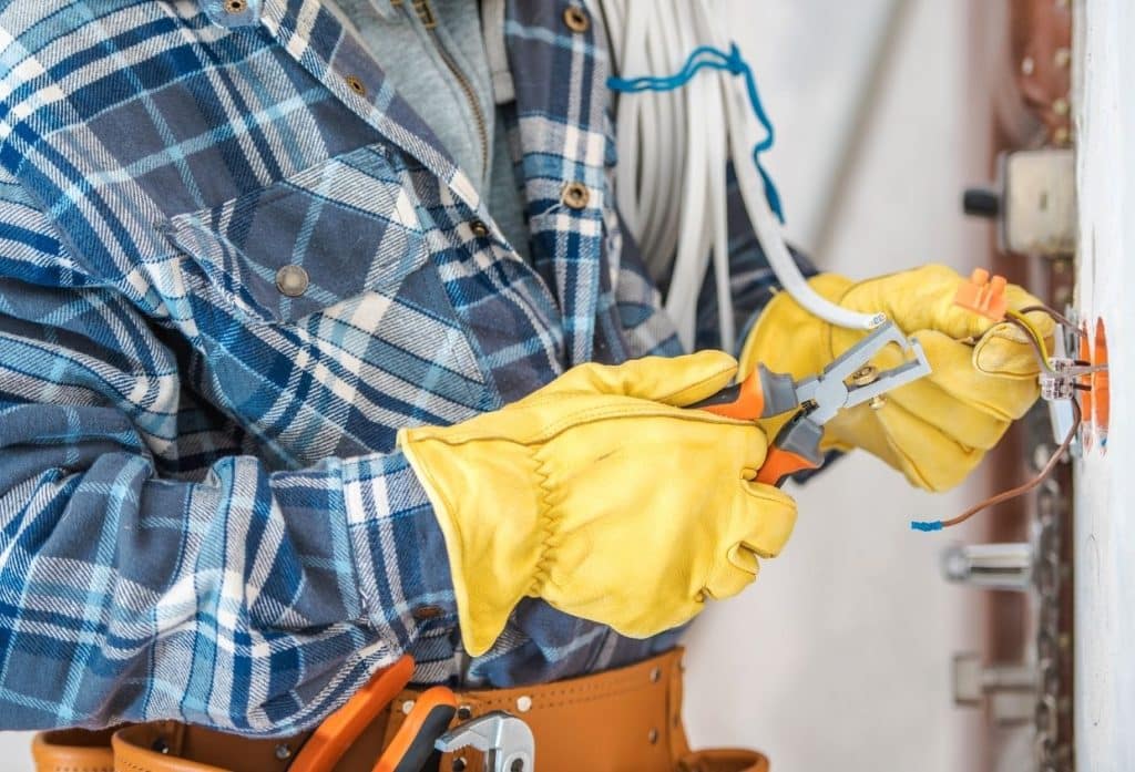 Electrician repairing and securing electrical wiring with insulated tools and gloves.