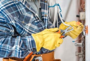 Electrician repairing and securing electrical wiring with insulated tools and gloves.