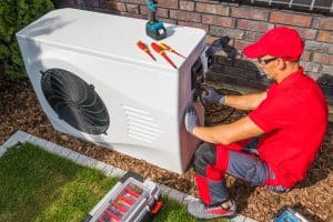 HVAC technician repairing an outdoor heat pump unit with tools and a toolbox nearby.